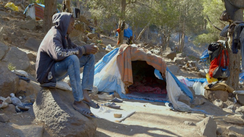 Один из живущих в лагере мальчишек сидит у своей палатки, ожидая ​​шанса на попытку перехода. (Изабелла Александр / GlobalPost).